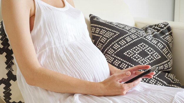 Zwangere vrouw surft op internet met smartphone zittend op de bank thuis close-up