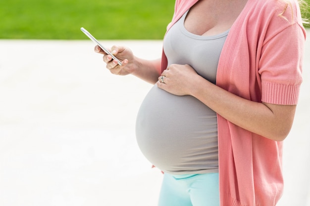 Zwangere vrouw wat betreft haar buik en texting die zich buiten bevindt