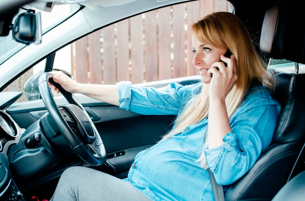 Zwangere vrouw zitten in de auto met behulp van mobiele telefoon op de parking. mooie zwangere vrouw met pauze van het rijden voor noodoproep