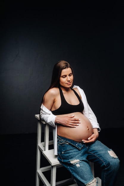 Zwangere vrouw zittend op een ladderstoel in een studio op een zwarte achtergrond.