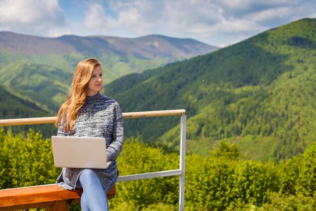 Zwangere vrouw zoekt iets in haar laptop op een bankje op de achtergrond van de natuur