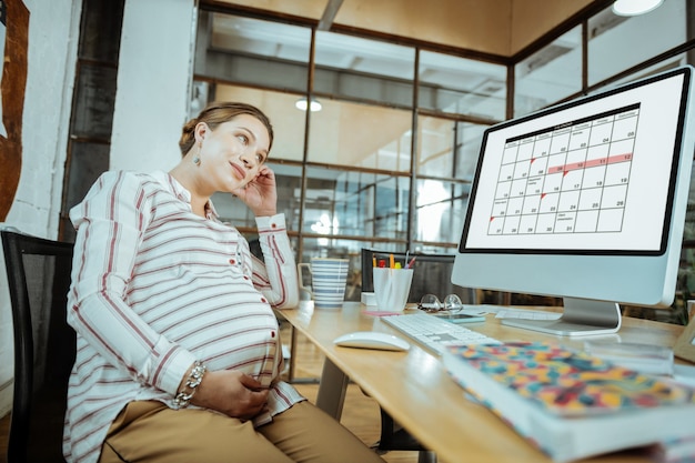 Zwangere vrouw zwangere volwassen vrouw in dienst die achter de computer zit en het schema controleert