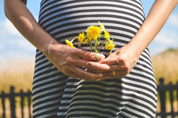 Foto zwangere vrouwenhanden geven gele wilde bloemen met zonnige weide en blauwe hemel