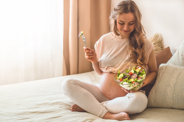 Zwangerschap en gezonde biologische voeding. Zwangere vrouw die van verse groentesalade in bed, vrije ruimte geniet