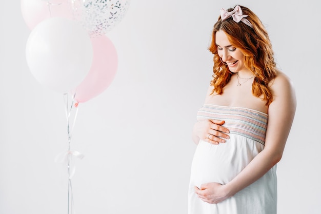Zwangerschap model schieten Gelukkige vrouw Verwacht nieuw leven Moederschap schoonheid Glimlachende buik dame aanraken baby bump geïsoleerde witte pastel ballonnen decoratie kopie ruimte