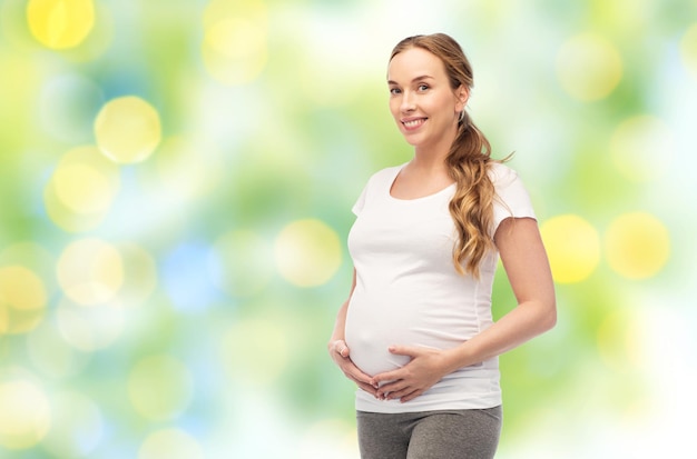 zwangerschap, moederschap, mensen en verwachtingsconcept - gelukkige zwangere vrouw die haar grote buik aanraakt over zomer groene lichten achtergrond