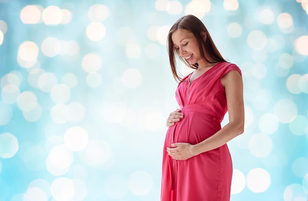 zwangerschap, moederschap, mensen en verwachtingsconcept - gelukkige zwangere vrouw met grote buik over blauwe vakantie steekt achtergrond aan