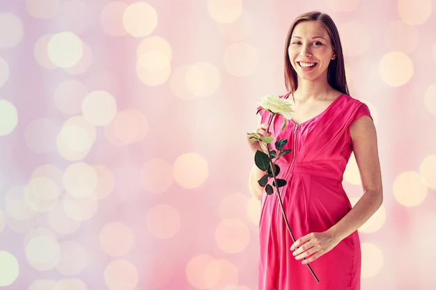 zwangerschap, moederschap, mensen, vakantie en verwachtingsconcept - gelukkige zwangere vrouw met witte roze bloem over roze vakantie steekt achtergrond aan