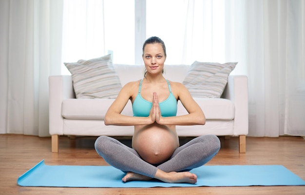 Zwangerschap, sport, yoga, mensen en gezond levensstijlconcept - gelukkige zwangere vrouw die thuis mediteren