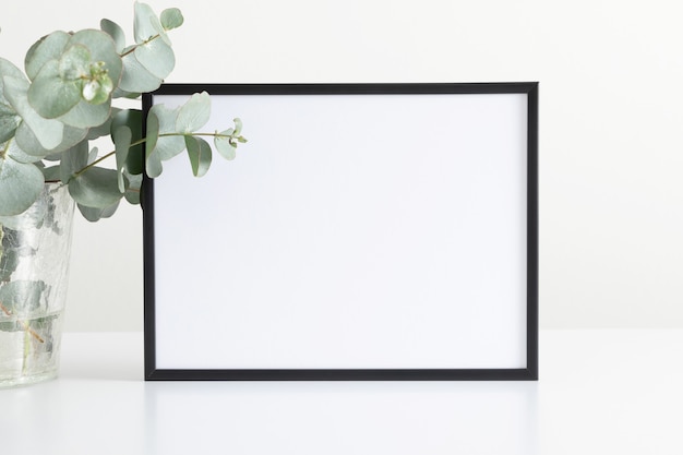 Foto zwart framemodel en eucalyptusbladeren in vaas op witte tafel vooraanzicht