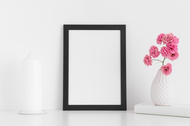 Zwart framemodel met roze rozen in een vaas en kaars op een witte tafel Portretoriëntatie