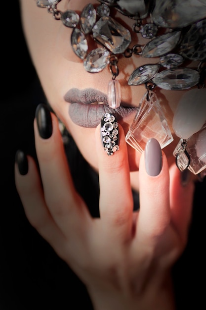 Zwart grijze glam matte make-up en manicure met strass steentjes en decoratie op het gezicht van het meisje close-up.