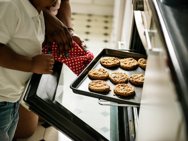 Zwart jong geitje die mamma helpen die koekjes in de keuken bakken