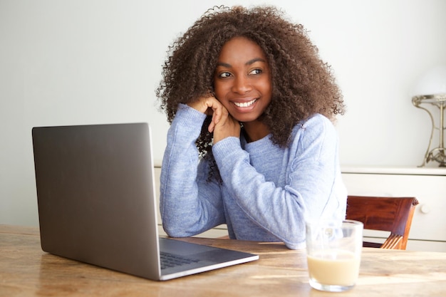 Zwart meisje zit aan een tafel met een laptop en kijkt weg en glimlacht