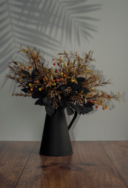 Zwart metalen vaas met bloemen op een witte ondergrond en een houten ondergrond