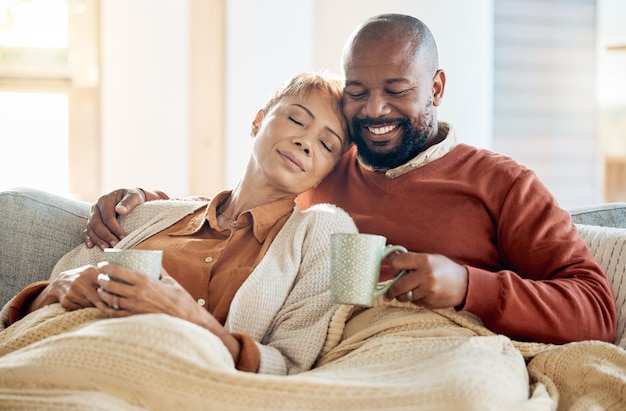 Zwart paar ontspannen op de bank met een koffiedeken en glimlachen op de winterweekendochtend in huis Vrede, comfort en liefde gelukkige man en vermoeide vrouw gezellige tijd op de bank met een drankje in de woonkamer samen