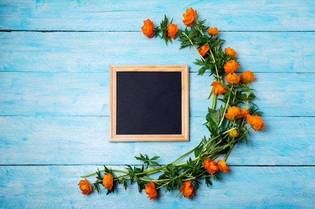 Zwart schoolbord houten vierkant frame mockup met globeflowers op de blauwe tafel leeg schoolbord frame mock up voor presentatieontwerp sjabloon zwart vilt briefbord inlijsten voor moderne kunst