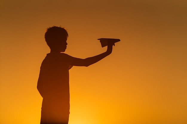 Zwart silhouet van een jongen die zich tegen de oranje achtergrond van de de zomerzonsondergang bevindt