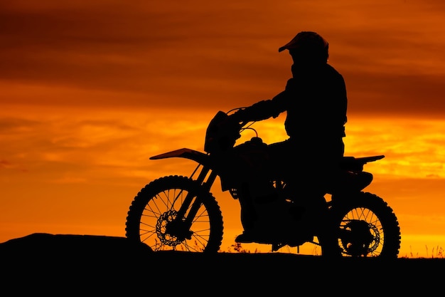 Zwart silhouet van fietser met motobike op oranje zonsonderganghemelachtergrond