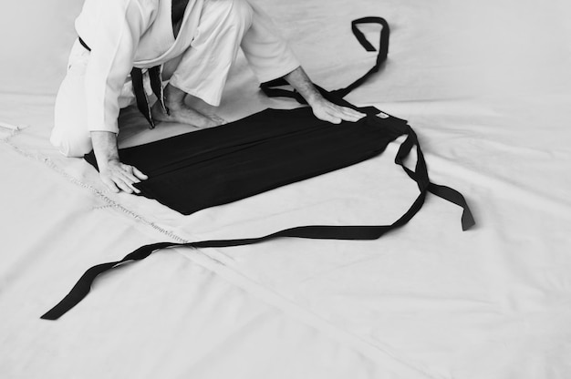 Zwart-wit afbeelding van aikido de mannelijke atleet vouwt zorgvuldig de zwarte hackam de traditionele vorm van kleding in aikido