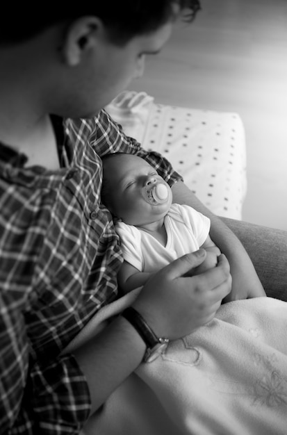 Zwart-wit beeld van schattige babyjongen viel in slaap op vaders handen