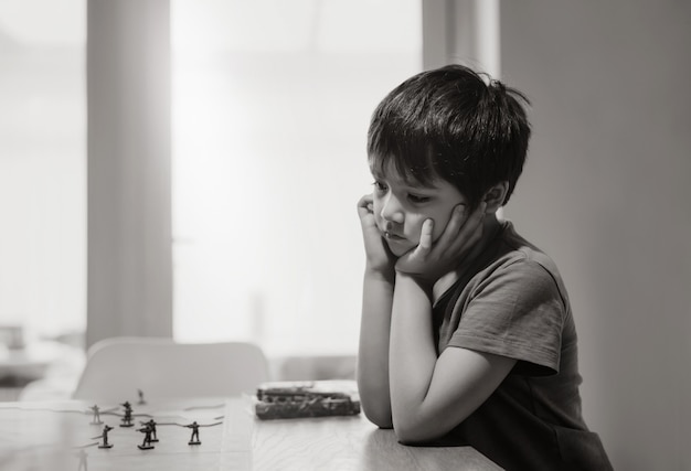 Zwart-wit Emotioneel portret van trieste jongen die alleen zit en speelt met tankspeelgoed