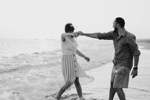 Zwart-wit foto jong romantisch koppel dansen ronddraaien door zee