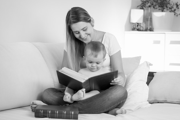 Zwart-wit portret van een jonge moeder die een boek leest aan haar baby