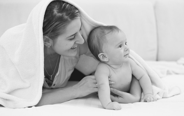 Zwart-wit portret van gelukkige jonge moeder die met haar zoon van 6 maanden op bed ligt