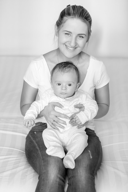 Zwart-wit portret van jonge lachende moeder zittend met haar 3 maanden oude baby