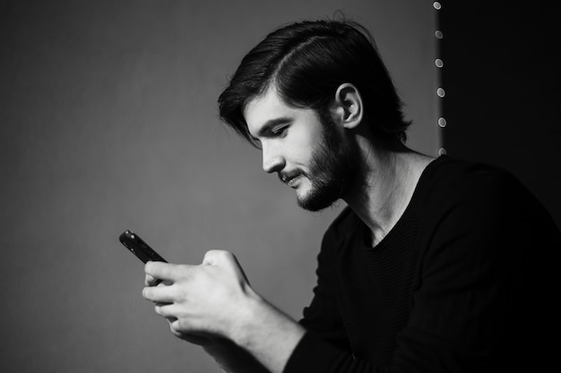 Zwart-wit portret van jonge man met smartphone in de hand.