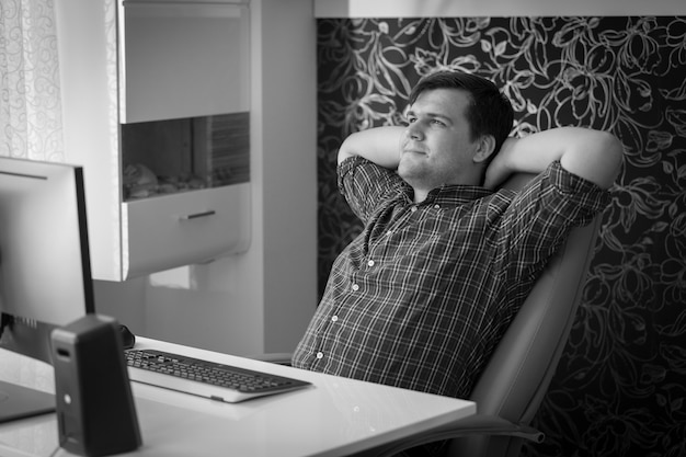 Zwart-wit portret van jonge man ontspannen op stoel op kantoor tijdens pauze