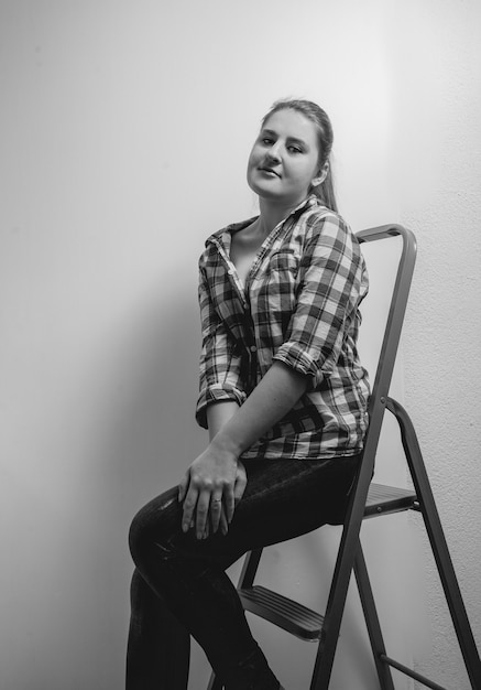 Zwart-wit portret van mooie lachende vrouw in shirt zittend op ladder