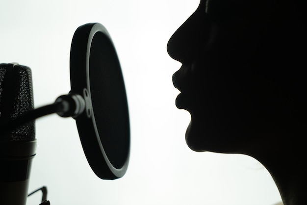 Zwart-wit profiel van een jonge vrouw die aan de ronde microfoon zingt Close-up van het gezicht van een vrouw in de buurt van de microfoon