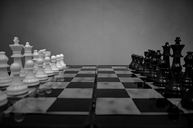 Zwart-wit schaakstukken tegenover elkaar op schaakbord op grijze achtergrond