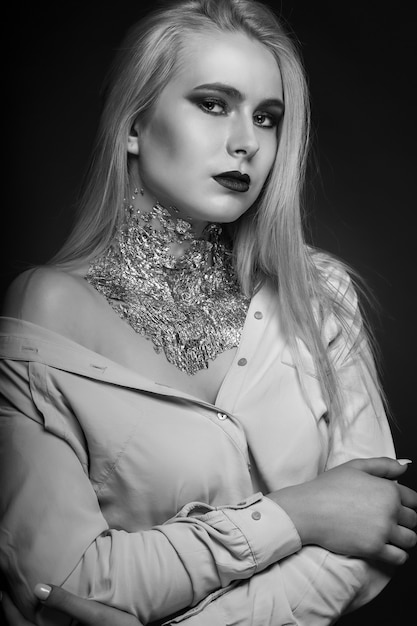 Zwart-wit schoonheidsshoot: glorieus blond model poseren in studio met lichte make-up en folie op haar nek