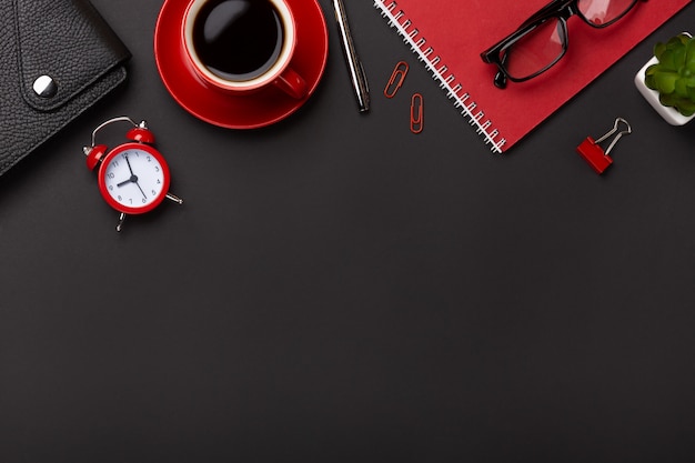 Zwarte achtergrond rode koffiekop notepad wekker bloem dagboek scores toetsenbord op de tafel. Bovenaanzicht met kopie ruimte