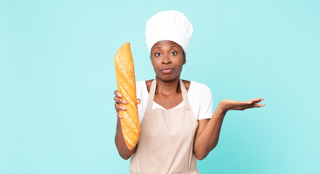 Zwarte Afrikaanse Amerikaanse volwassen chef-kokvrouw die een broodbaguette houdt