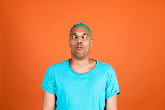 Zwarte afrikaanse man in casual op oranje muur blauw haar doet grappige gekke grimassen visgezicht met plezier