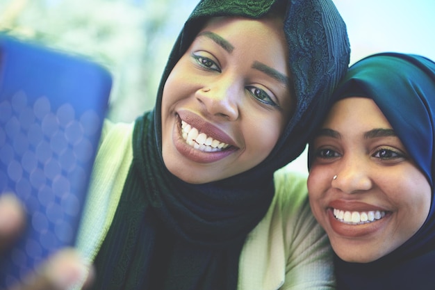 zwarte Afrikaanse vrouwelijke vrienden die samen een smartphone gebruiken en traditionele islamitische hijab-kleding dragen