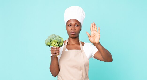 Zwarte Afro-Amerikaanse volwassen chef-kokvrouw die een broccoli houdt