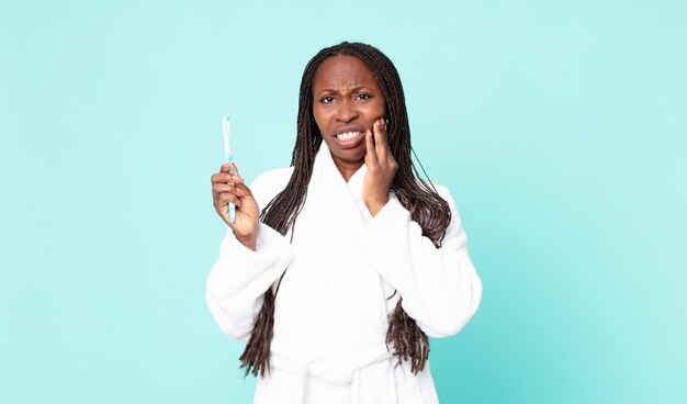 Zwarte afro-amerikaanse volwassen vrouw die een badjas draagt en een tandenborstel vasthoudt