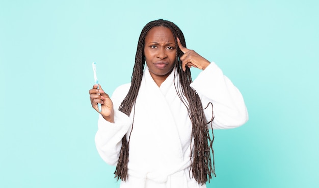 Zwarte afro-amerikaanse volwassen vrouw die een badjas draagt en een tandenborstel vasthoudt