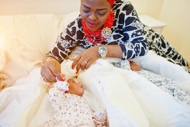 Zwarte Afro-Amerikaanse vrouw gekleed in traditionele etnische kleding die naast haar kleine baby's op het bed ligt