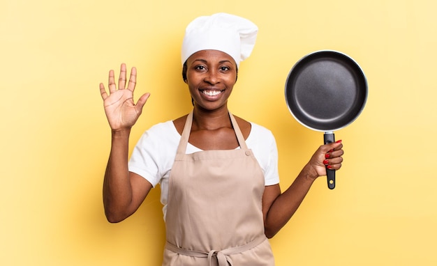 Zwarte afro-chef-vrouw die lacht en er vriendelijk uitziet, nummer vijf of vijfde toont met de hand naar voren, aftellend