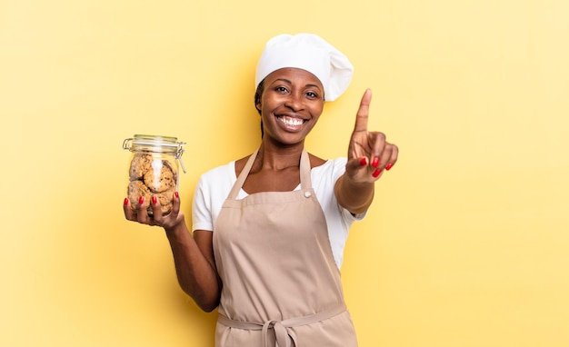 Zwarte afro-chef-vrouw die trots en zelfverzekerd glimlacht en nummer één triomfantelijk poseert, voelt zich een leider. koekjes concept