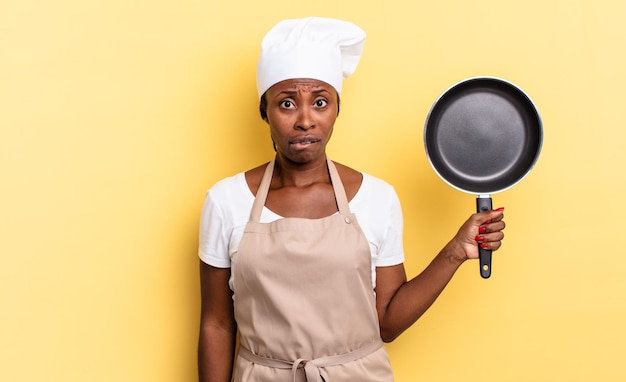 Zwarte afro-chef-vrouw die verbaasd en verward kijkt, lip bijt met een nerveus gebaar, niet wetend het antwoord op het probleem