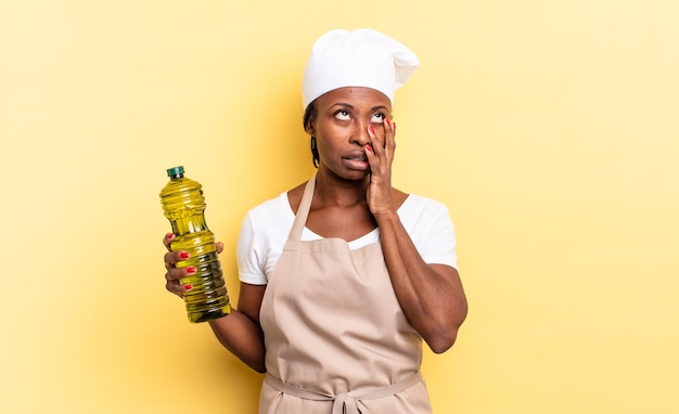 Zwarte afro-chef-vrouw die zich verveeld, gefrustreerd en slaperig voelt na een vermoeiende, saaie en vervelende taak, gezicht met de hand vasthoudend. olijfolie concept