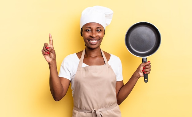 Zwarte afro-chef-vrouw lacht en ziet er vriendelijk uit, toont nummer één of eerste met hand naar voren, aftellend