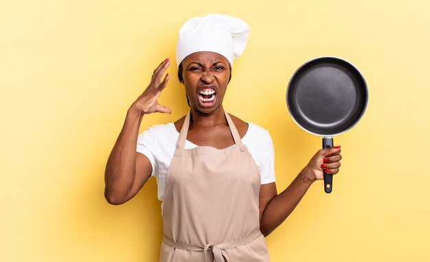 Zwarte afro-chef-vrouw schreeuwt met handen in de lucht, voelt zich woedend, gefrustreerd, gestrest en overstuur